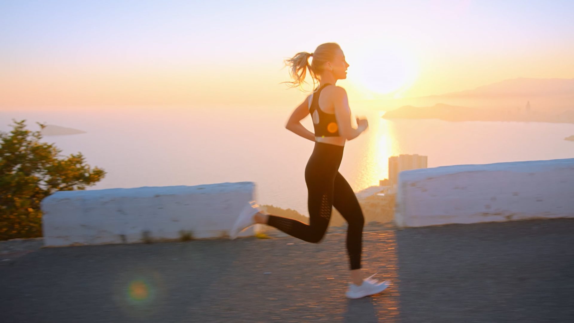 mujer corriendo al atardecer con ropa deportiva en carretera junto al mar