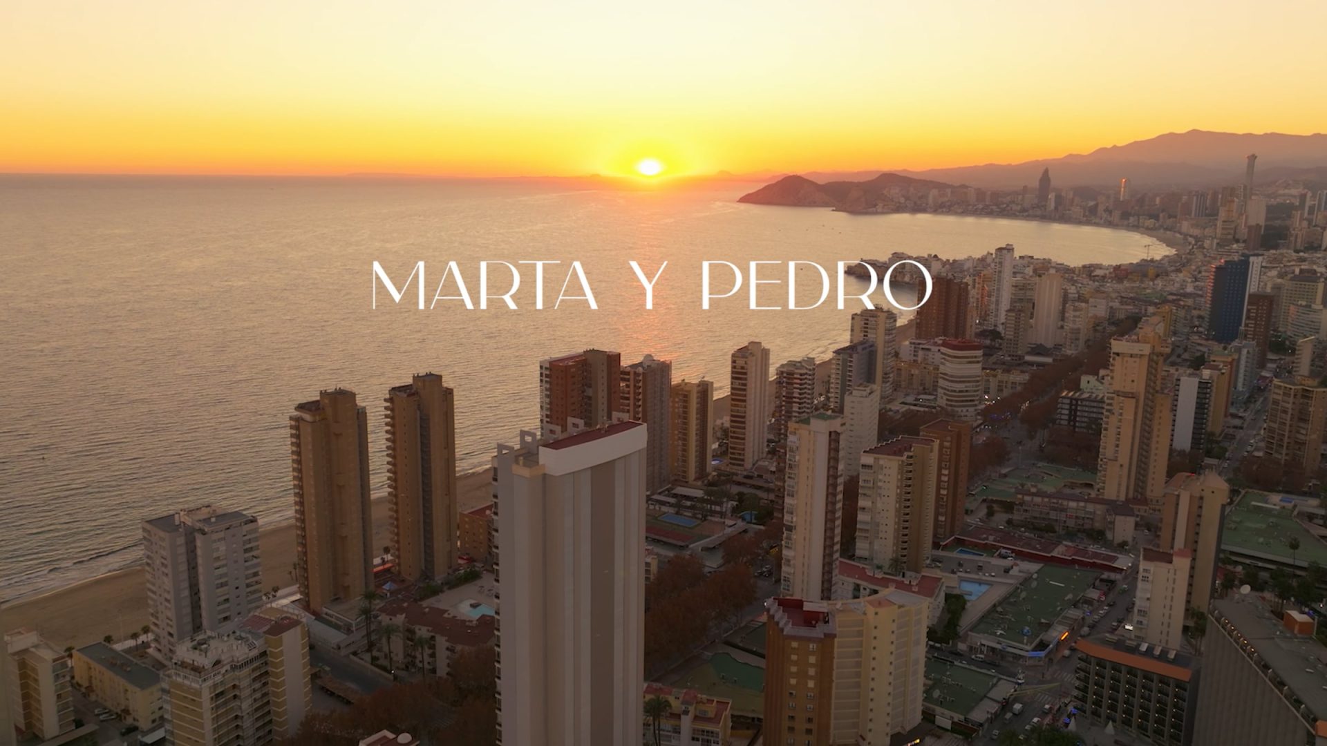 Vista aérea de la costa al atardecer con edificios y texto Marta y Pedro